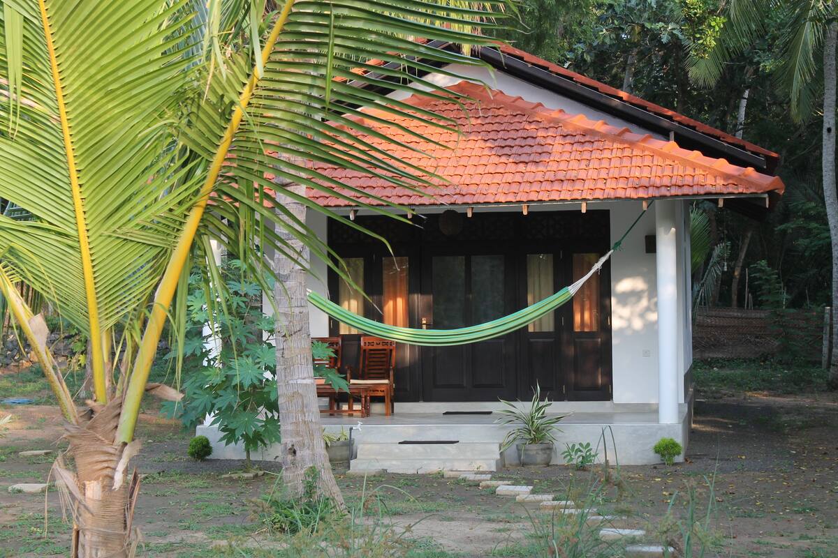 A small house with a tiled roof, a hammock, and a porch with chairs.