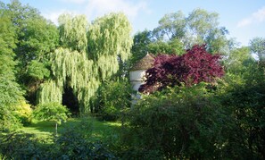 A garden with a variety of trees, including weeping willows and a red-leafed tree, and a small white building with a conical roof. - L'Ecrin du Serein (Sainte-Vertu)