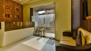 A modern reception area with a glass partition, a reception desk, and a seating area with a sofa and cushions.