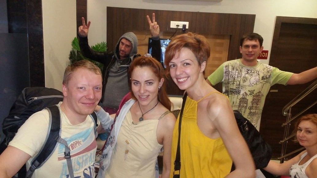 A group of people in a lobby with a staircase and a television screen in the background.