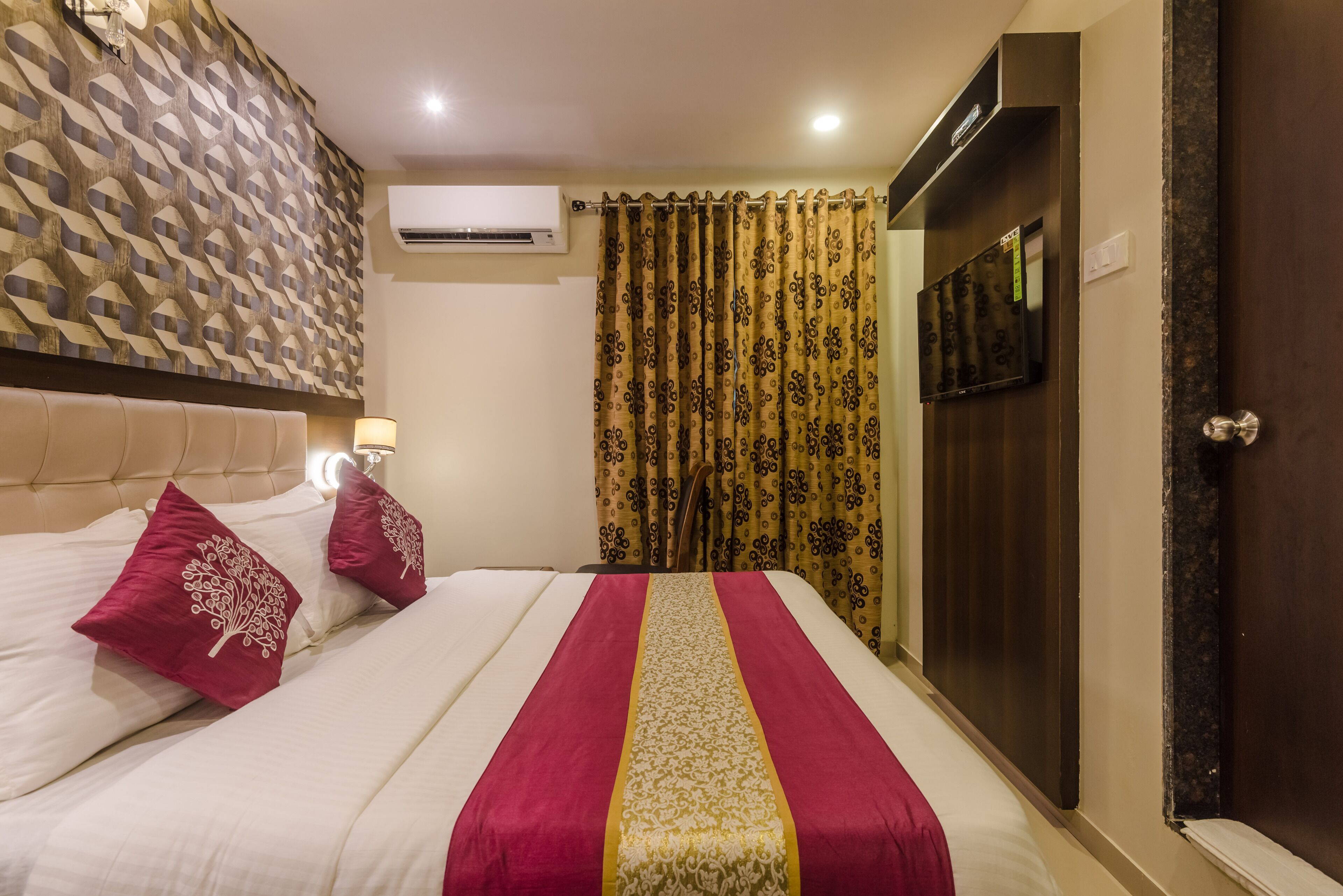 Une chambre d’hôtel avec un lit, une tête de lit, un climatiseur fixé au mur, un rideau et une porte.