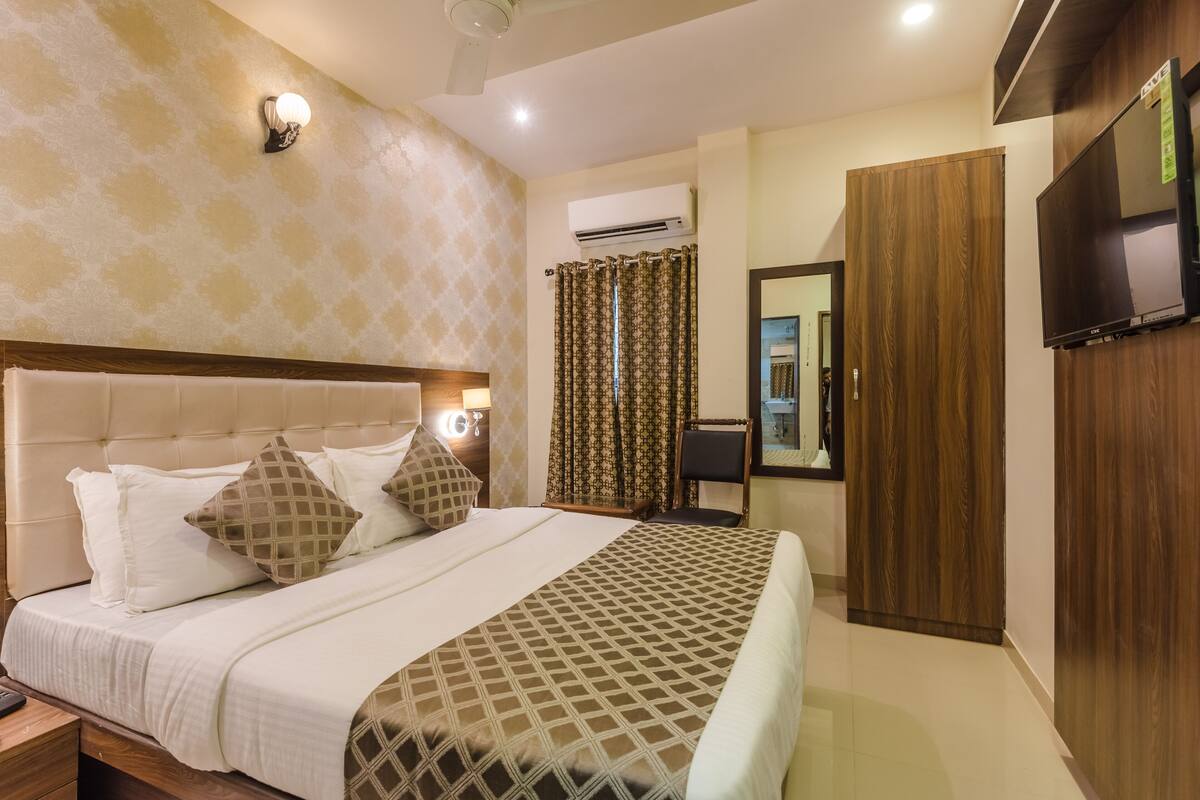 Una habitación de hotel con cama, mesita de noche, televisor, armario y aire acondicionado.