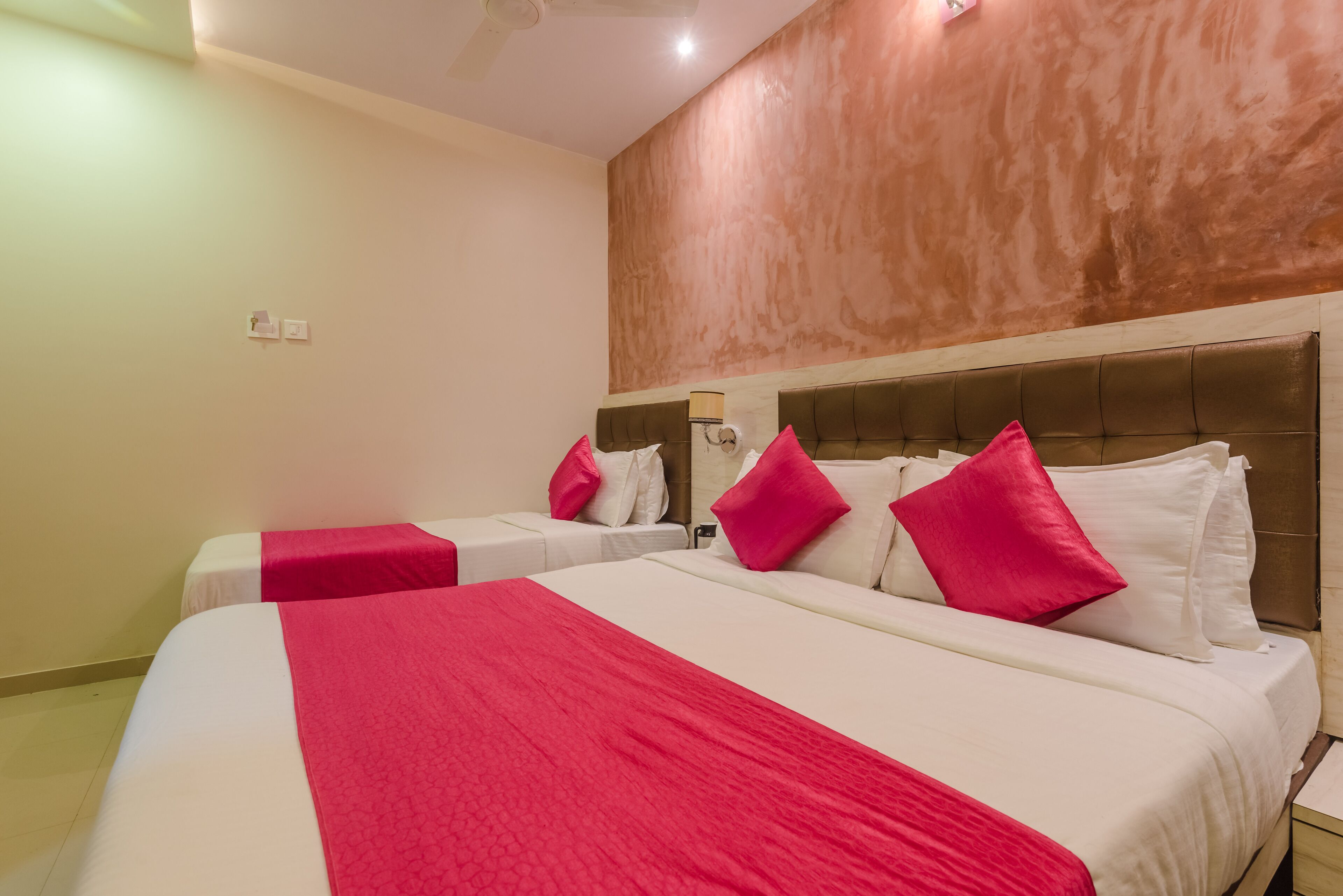 Habitación de hotel con dos camas, cada una con ropa de cama blanca y roja, un cabecero marrón y un ventilador de techo.