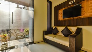 A modern living room with a sofa, a mounted TV, and a glass door leading to an outdoor area with a motorcycle and potted plants.