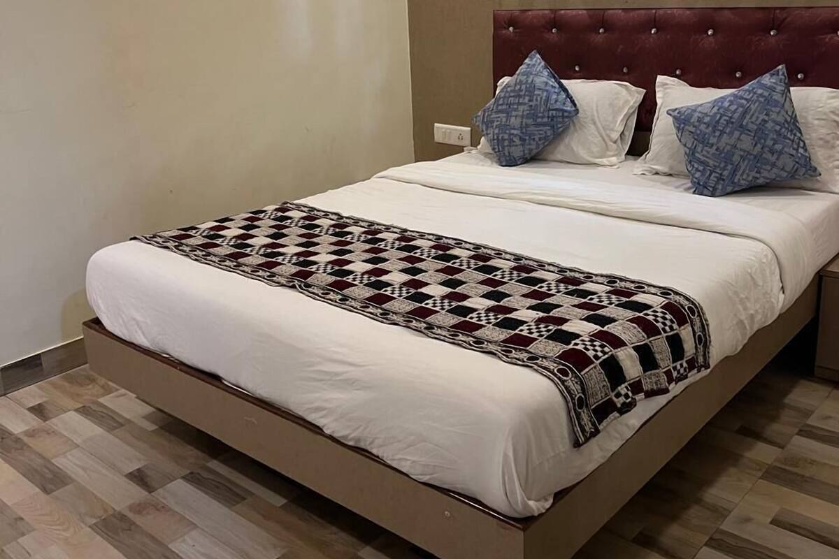 Una cama individual con un edredón estampado, dos almohadas, un cabecero y suelo de madera.