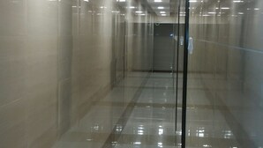 Un couloir doté d’un sol réfléchissant et de murs en verre, agrémenté de luminaires encastrés au plafond.