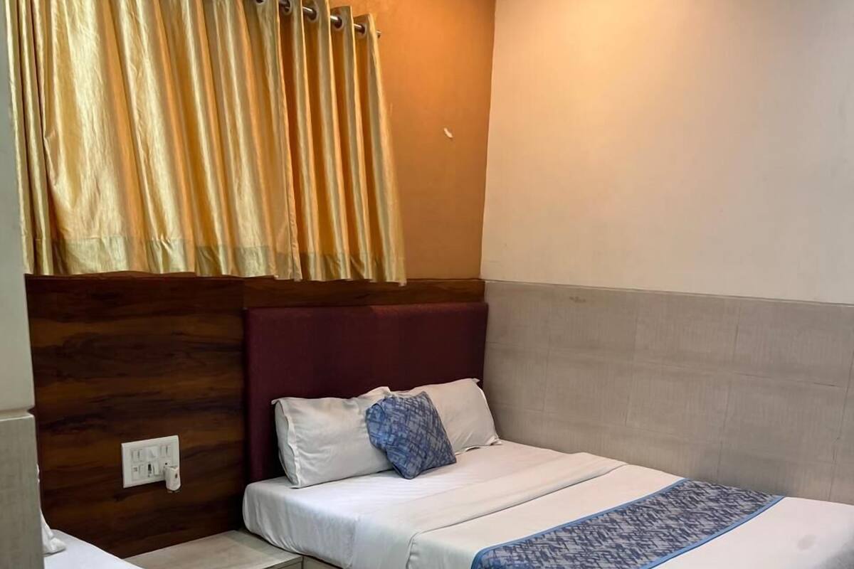 Una habitación de hotel con dos camas, cabecera de madera, ventana con cortinas y aire acondicionado instalado en la pared.