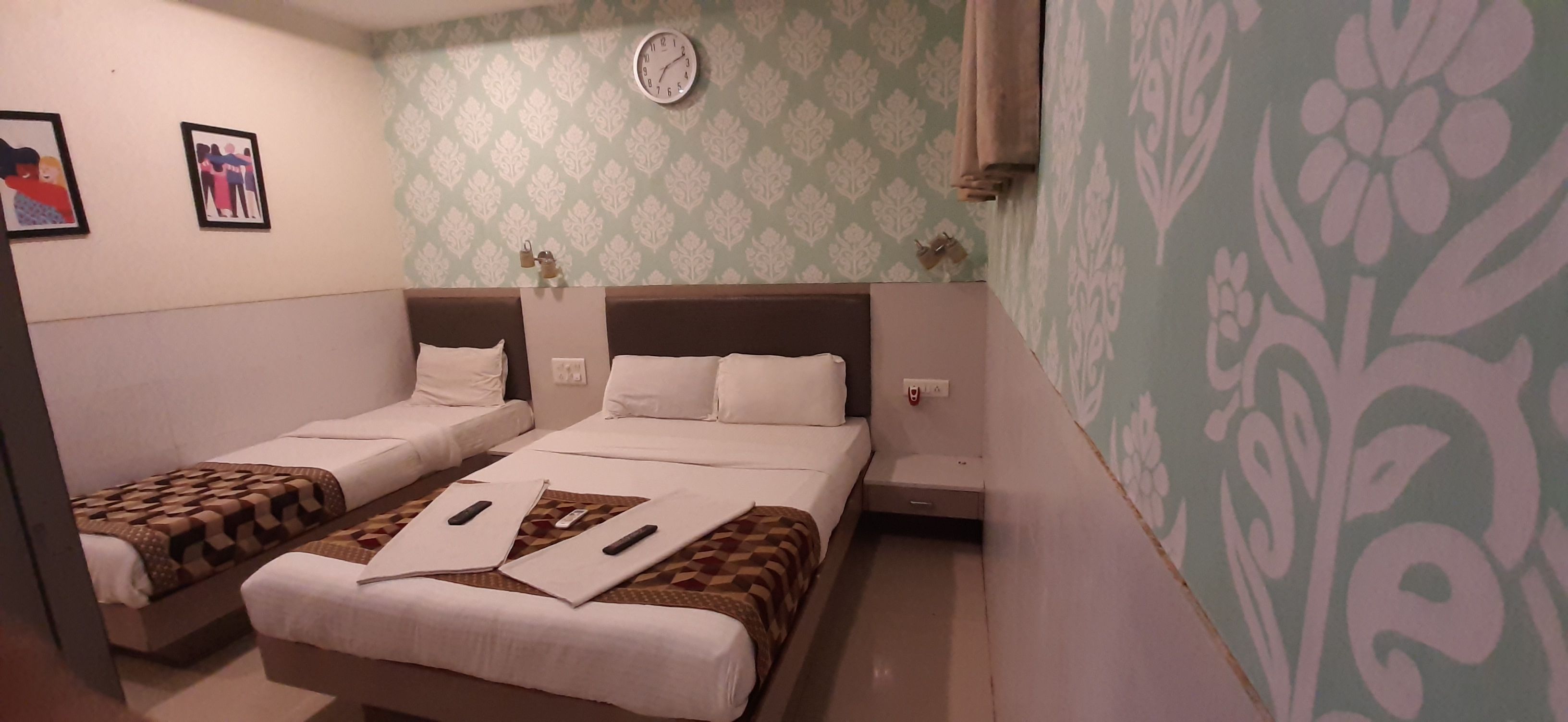A hotel room with two single beds, a clock on the wall, and patterned wallpaper.