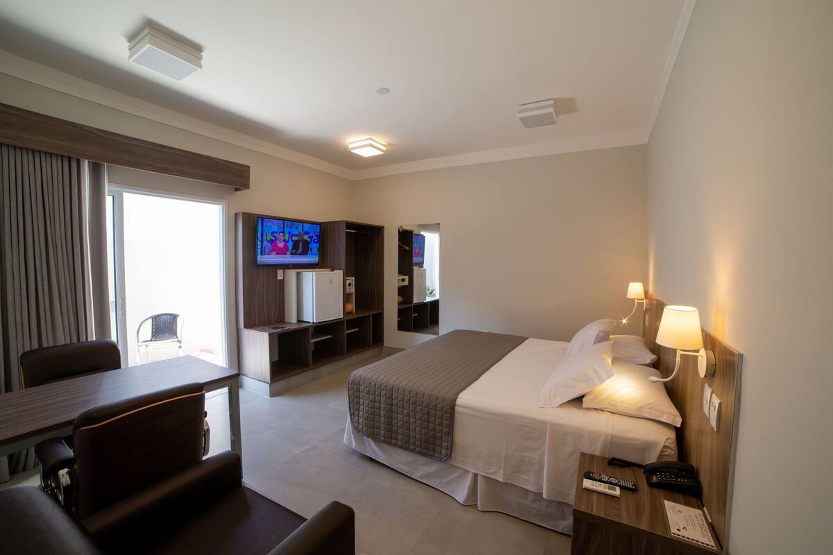 Une chambre d’hôtel comprenant un lit, une table de chevet, une lampe, une télévision et un bureau avec une chaise.