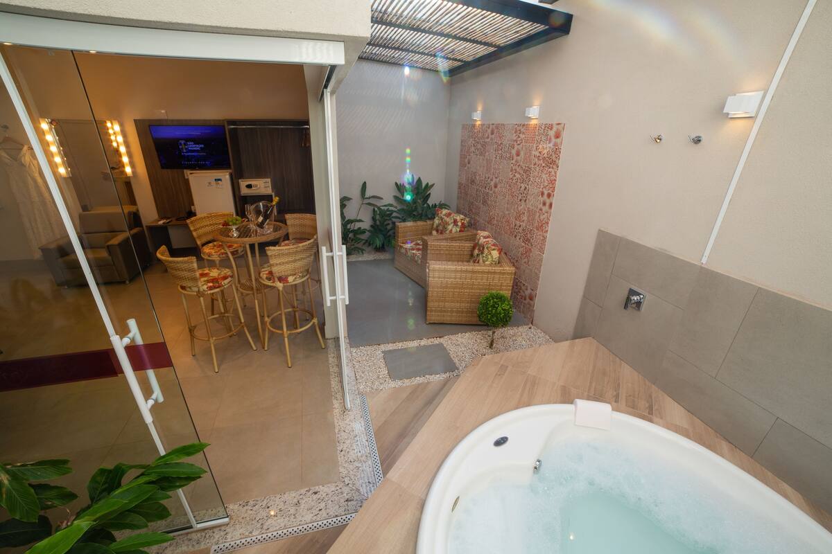 Une salle de bain moderne avec une grande baignoire, un coin salon avec des meubles en osier et un téléviseur en arrière-plan.