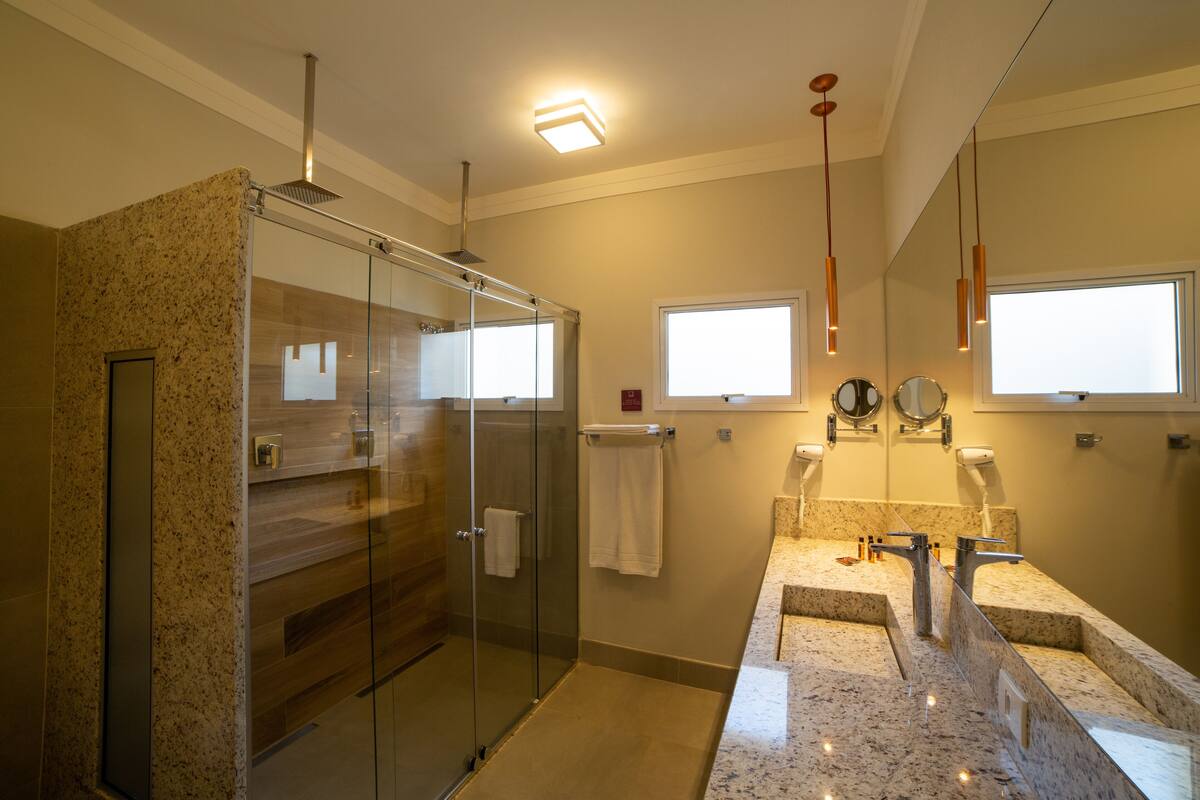Une salle de bain moderne dotée d’une douche à parois de verre, d’un meuble-lavabo avec un plan de travail en granit et d’un grand miroir au-dessus du lavabo.