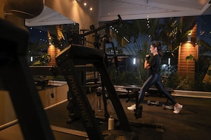 Un gimnasio con equipo de ejercicio, cinta de correr y una persona caminando.