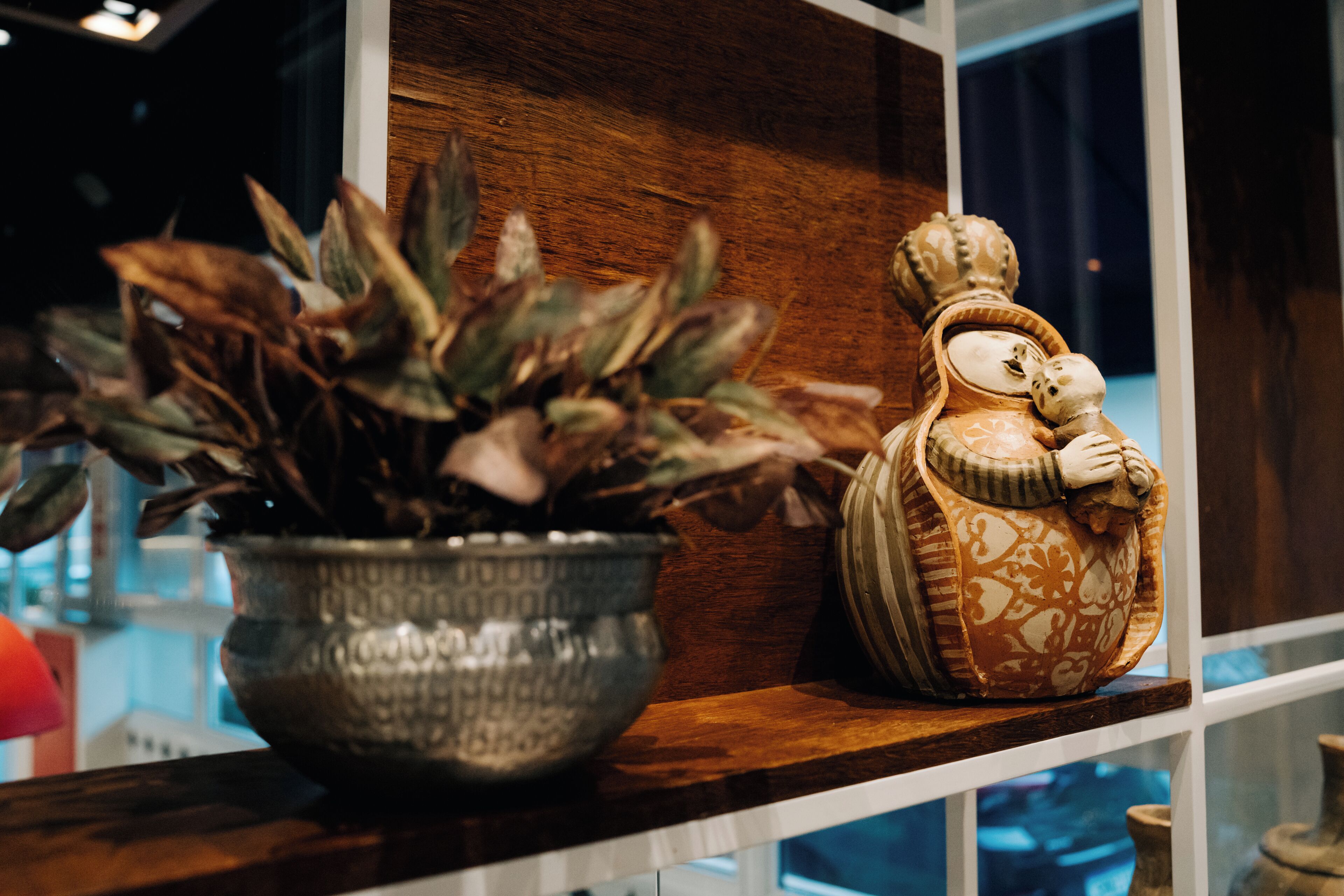 Un estante de madera con una planta en maceta y una figura decorativa de cerámica.