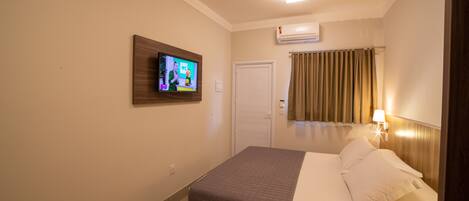 Habitación de hotel con cama, televisor montado en la pared, una puerta y una ventana con cortinas.