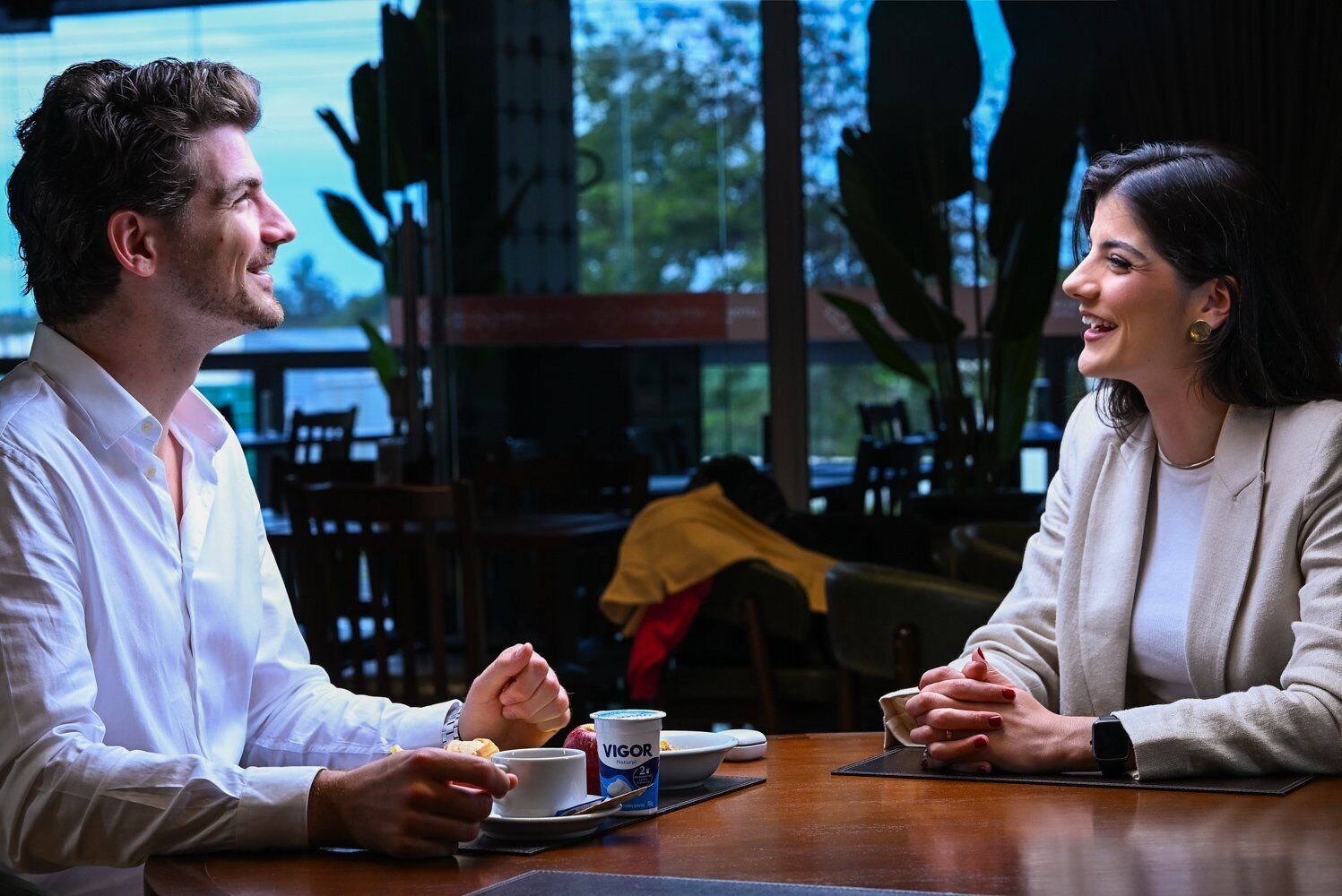 Two people seated at a table with a cup of coffee and a Vigor yogurt container.