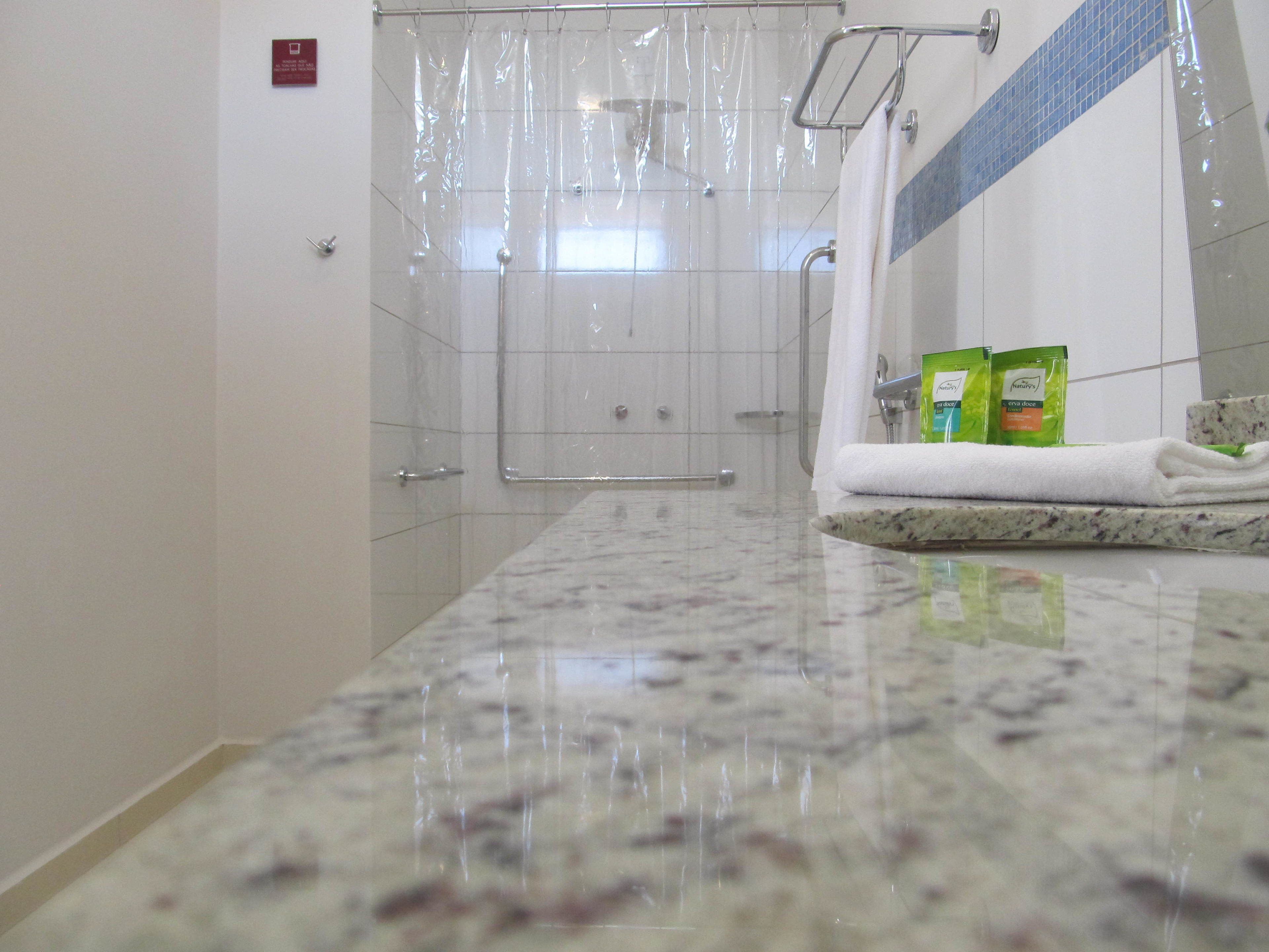 A bathroom with a shower, a marble countertop, and a towel rack with towels.