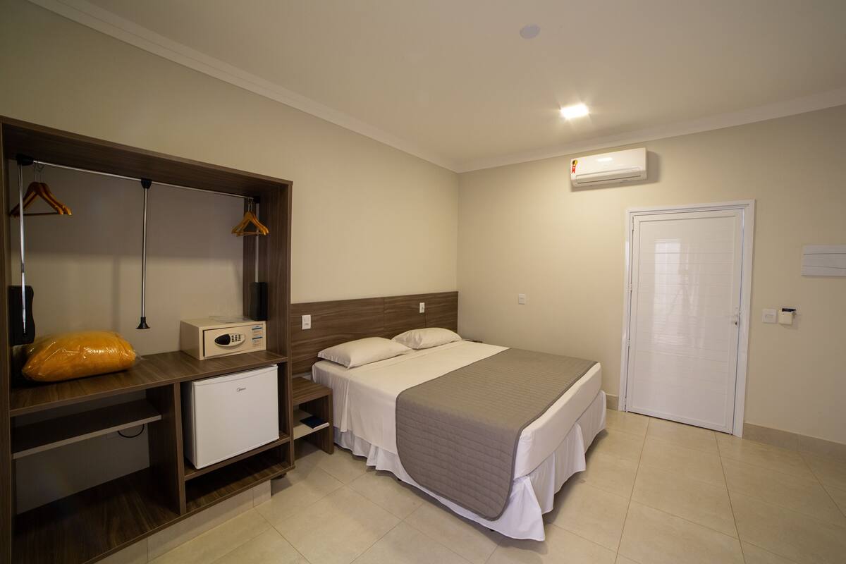 Une chambre d’hôtel comprenant un lit, un bureau avec un ordinateur, une armoire et un petit réfrigérateur.