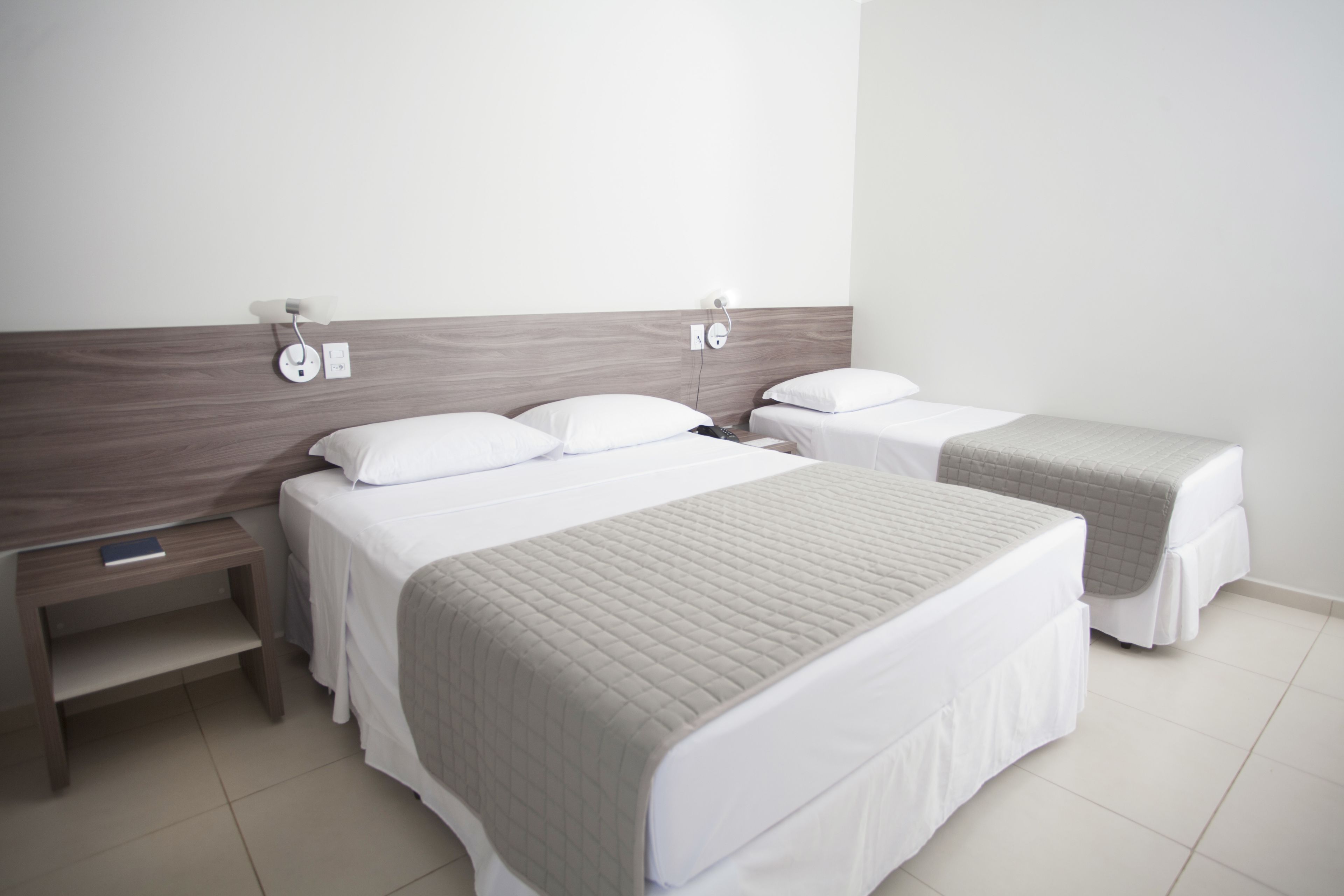 Habitación de hotel con dos camas, una mesita de noche y una lámpara de pared.