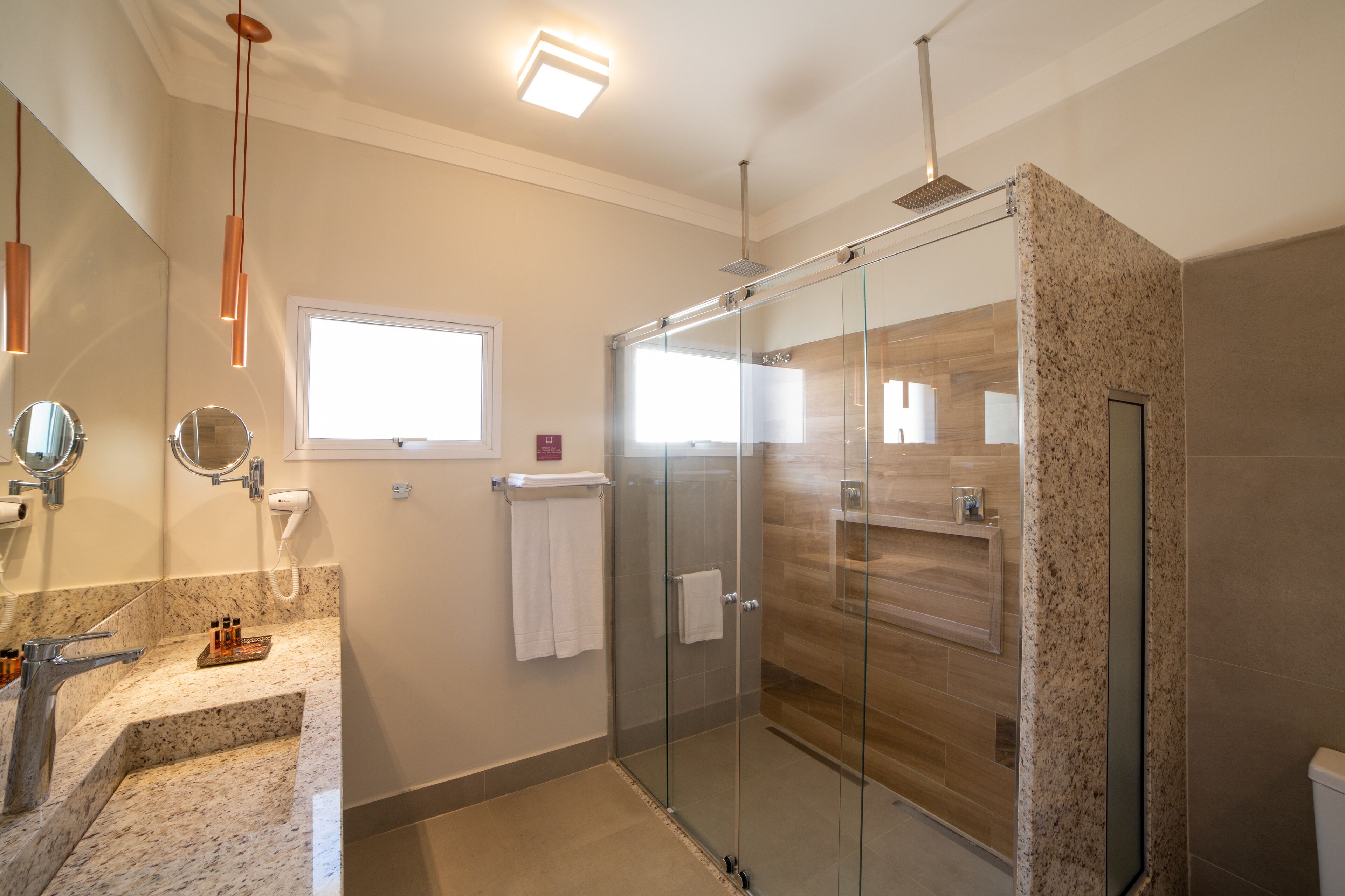 A modern bathroom with a glass-enclosed shower, a granite countertop, a vanity mirror, and a window providing natural light.