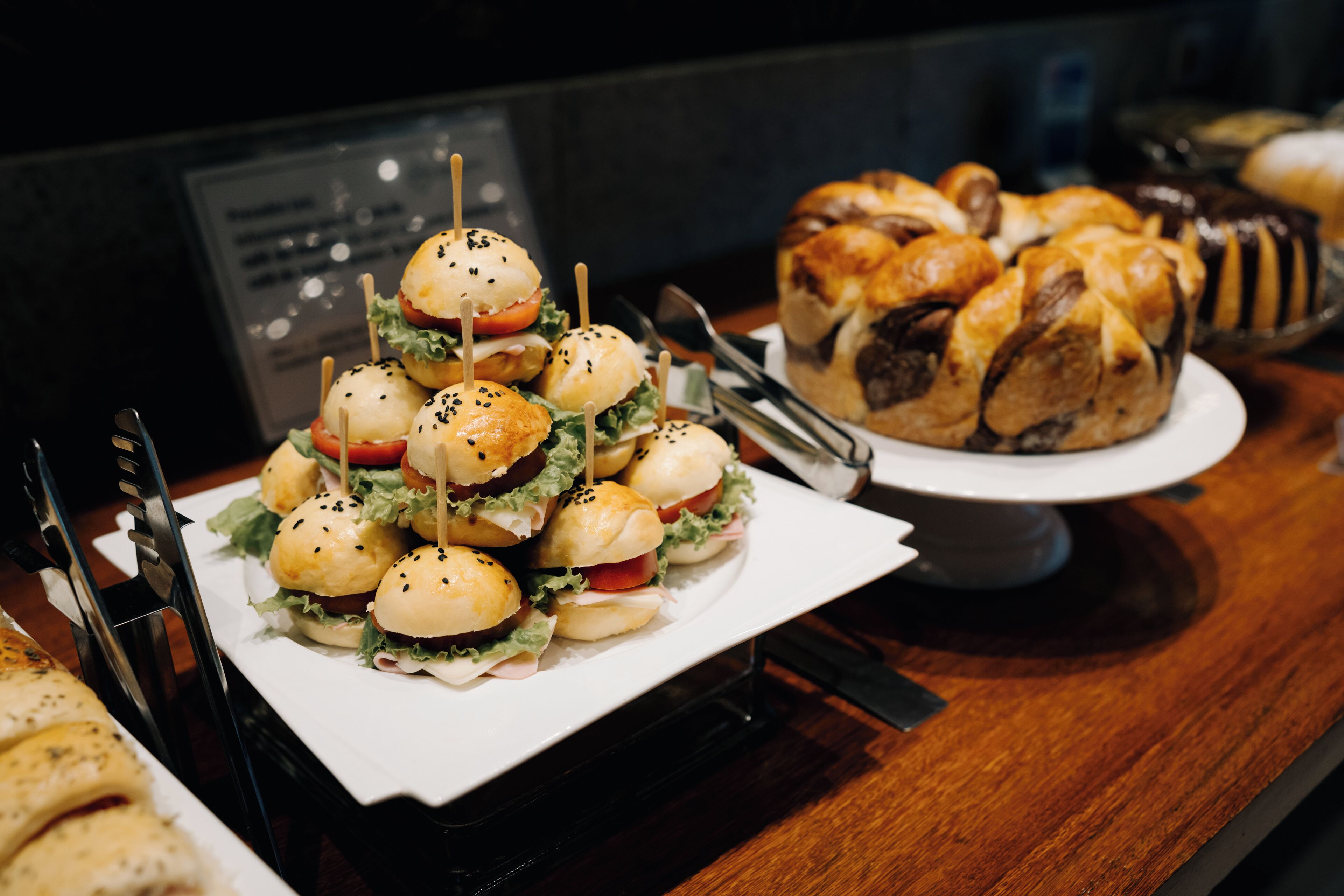 A buffet table with a variety of food items including sandwiches, pastries, and a display of bread rolls.