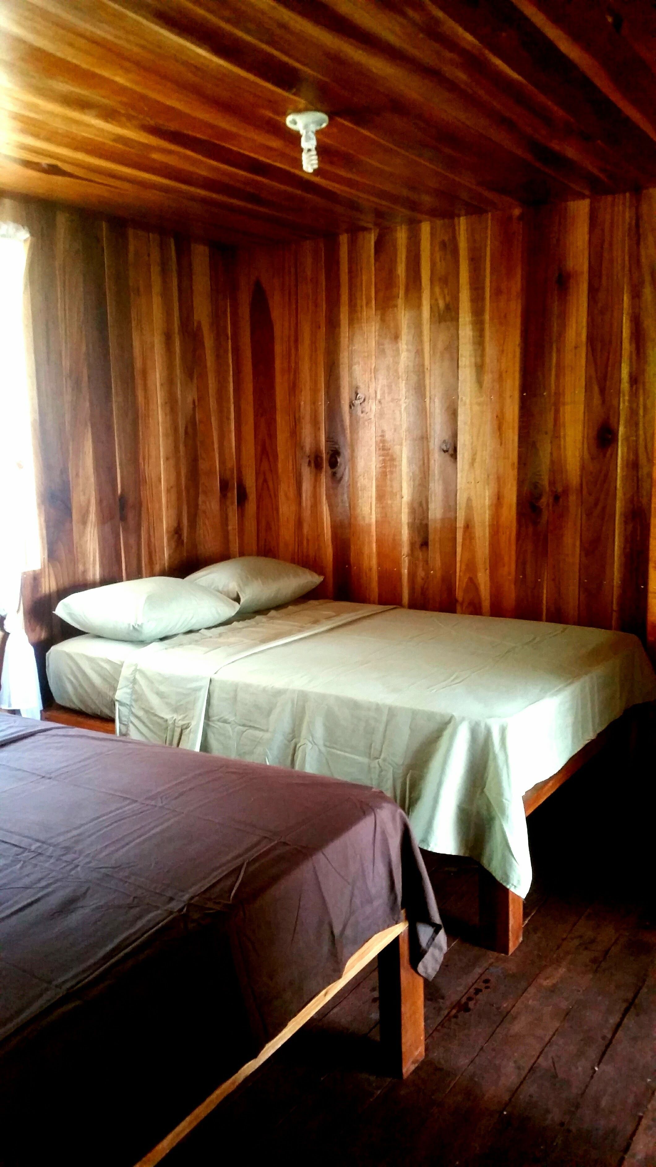 Habitación de cabaña de madera con dos camas, una con cubrecama verde y la otra con cubrecama marrón.