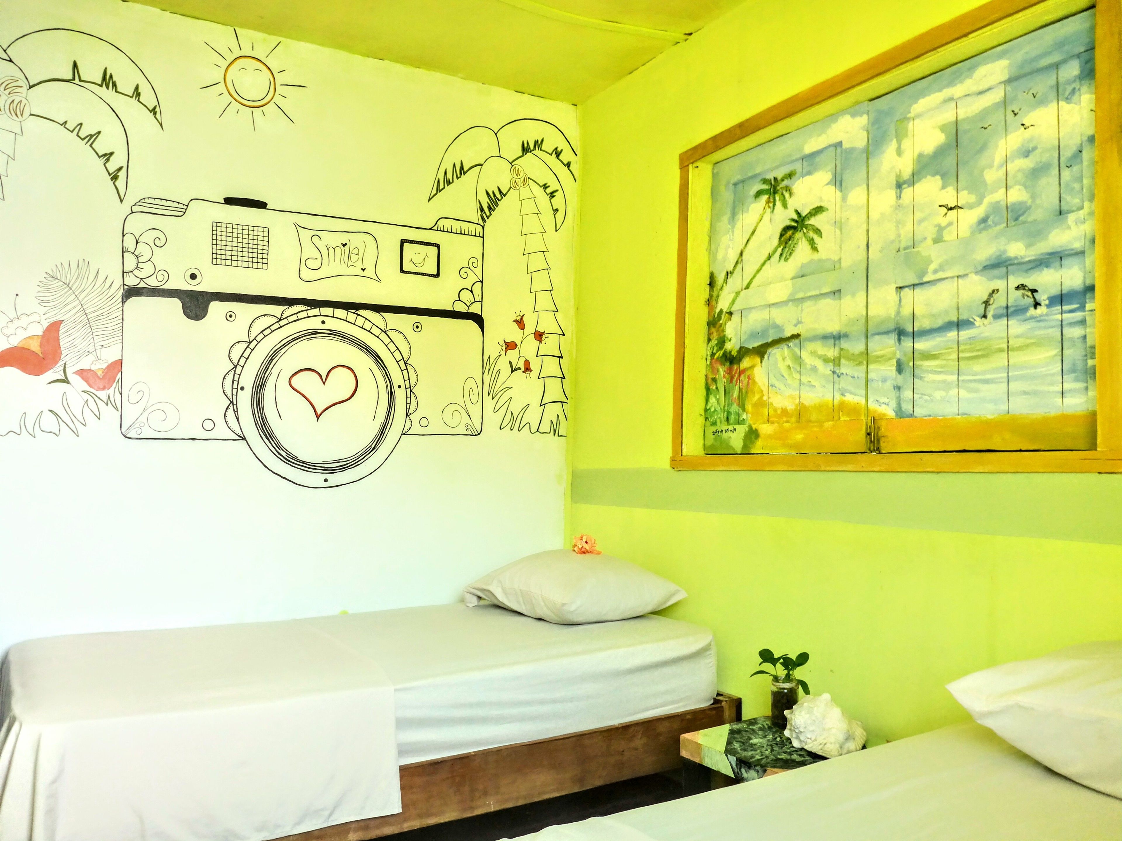 A room with a bed, a wall mural, and a window with a painting of a tropical scene.