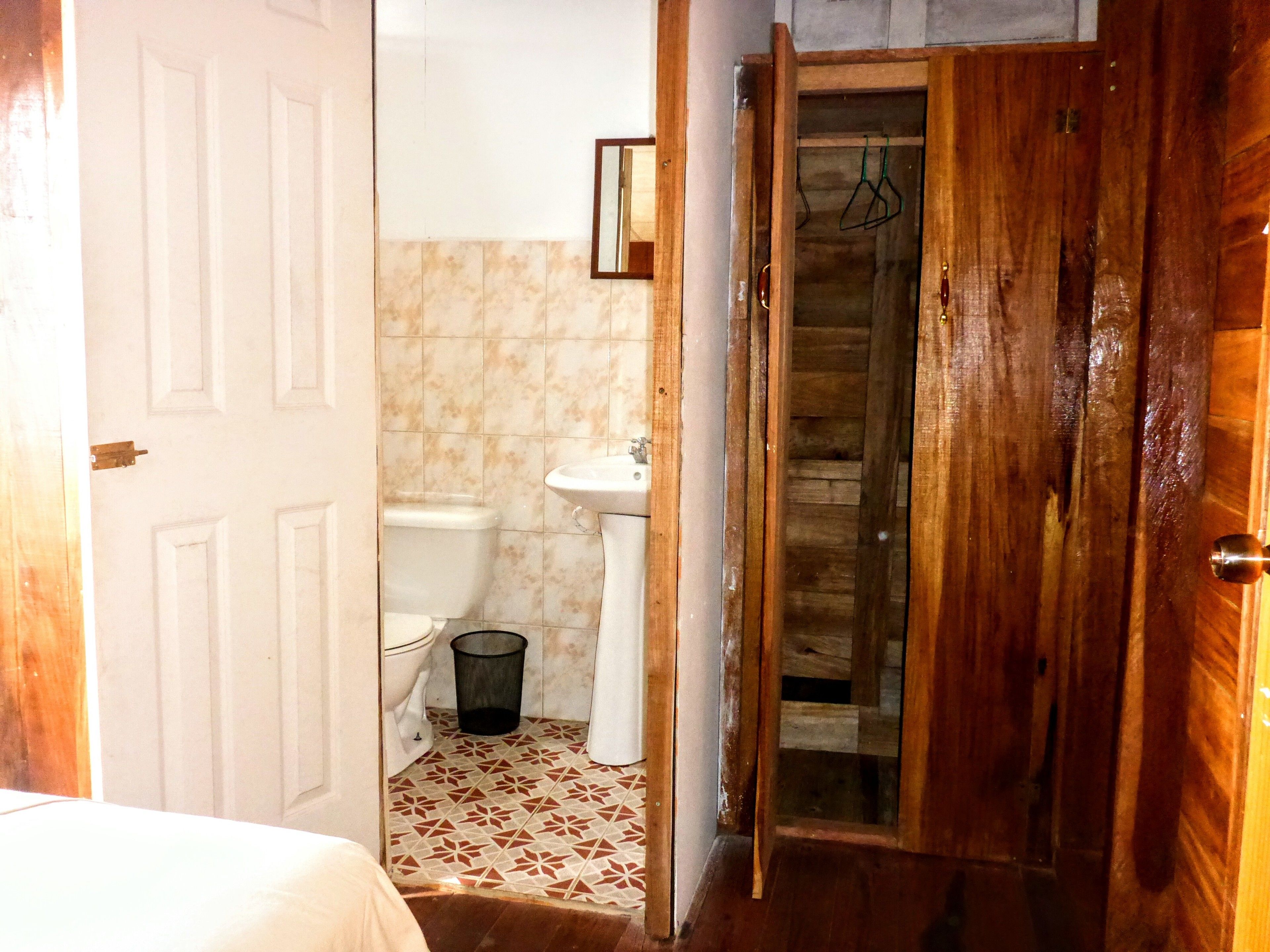 A narrow hallway with a wooden door, a white toilet, a sink, and a shower area.