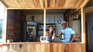 A wooden bar area with a menu board, a refrigerator stocked with drinks, and a clock on the wall. - El Jaguar (Bastimentos)
