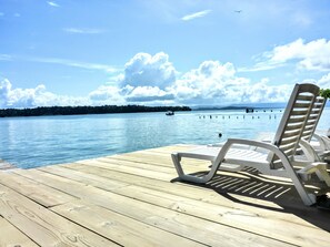 A wooden deck with white lounge chairs facing a calm lake, surrounded by trees and a clear sky. - El Jaguar (Bastimentos)