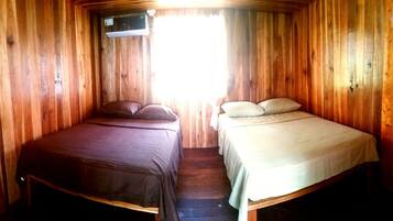 A wooden cabin room with two beds, one with dark bedding and the other with light bedding.