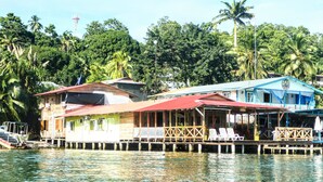 A waterfront property with a wooden structure, a covered area with chairs, and a blue building with a sign. - El Jaguar (Bastimentos)