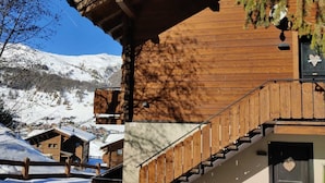 Una cabaña de madera con una escalera que lleva a un balcón, rodeada de montañas nevadas.