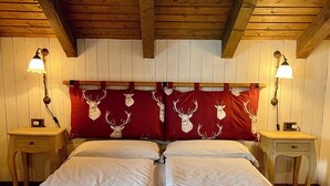 Una cama doble con sábanas blancas, cabecera de madera con cojines rojos y dos mesitas de noche con lámparas.