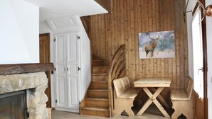 Una escalera de madera que conduce a una habitación con chimenea de piedra, bancos de madera y un cuadro de un ciervo.