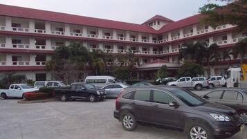 Un edificio de varios pisos con techo rojo y paredes blancas, que cuenta con un estacionamiento y varios automóviles.