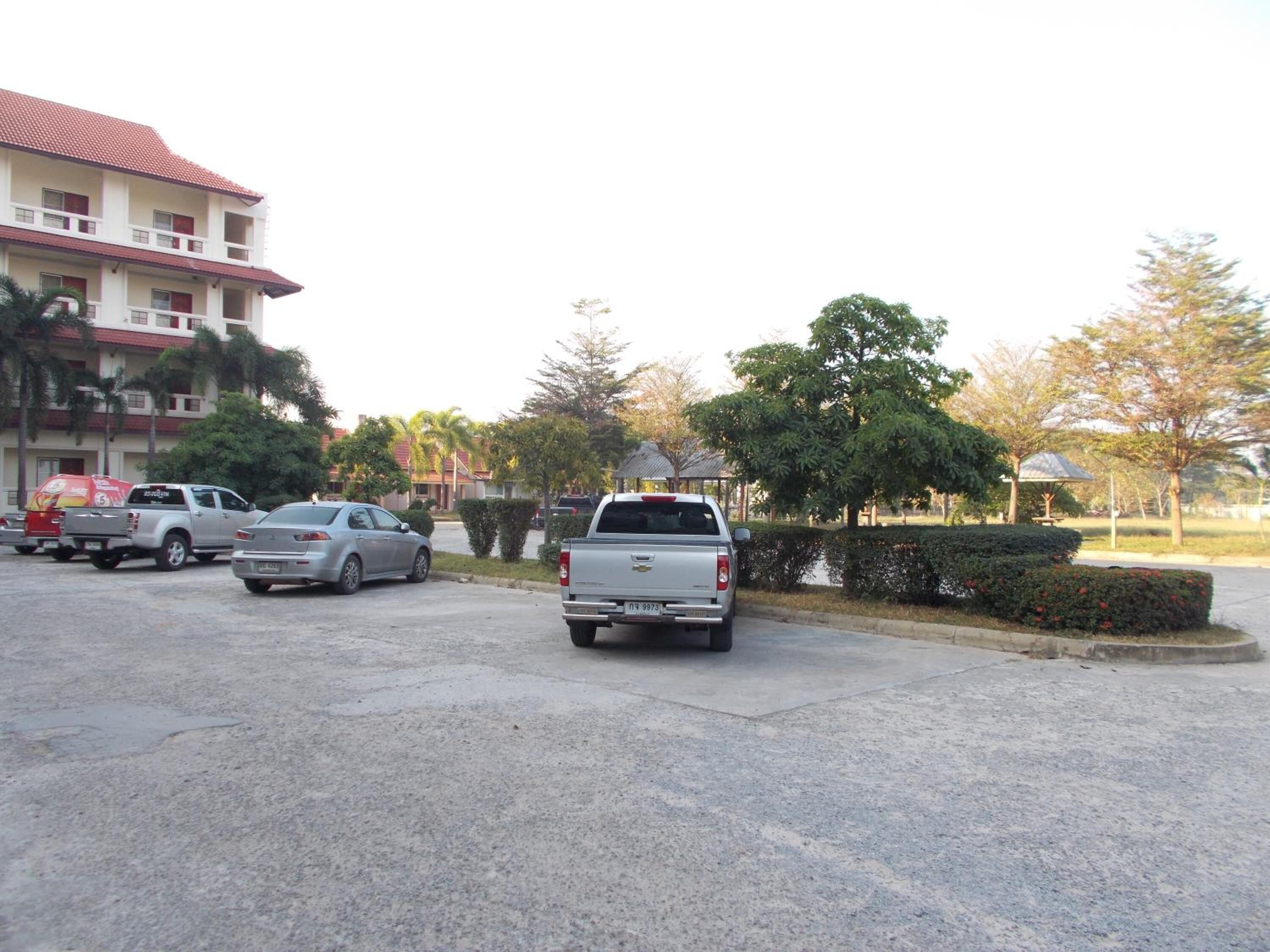 A parking lot with several parked vehicles, including a pickup truck and a sedan. There are buildings with red-tiled roofs in the background.