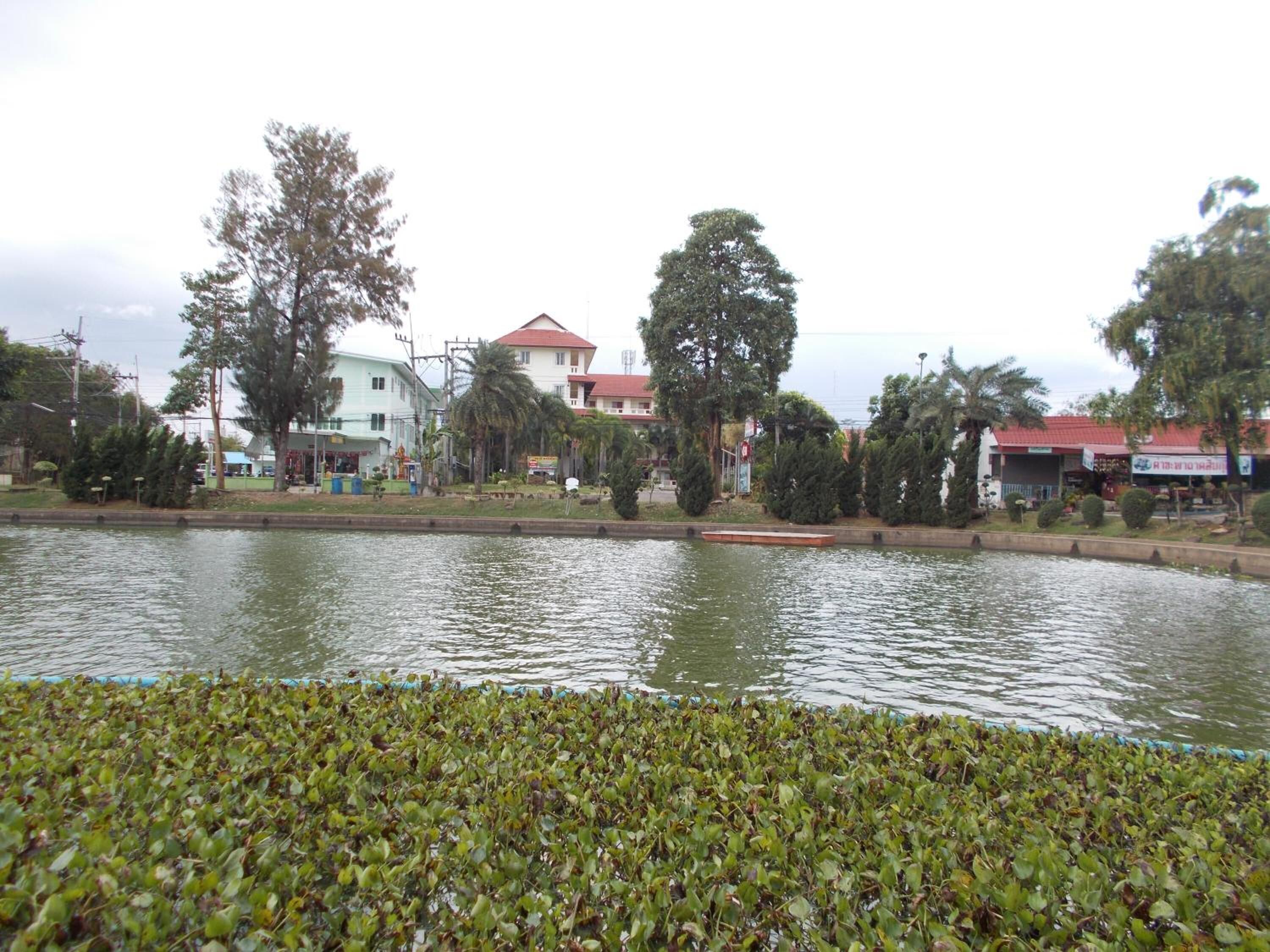 A calm water body with a floating dock, surrounded by greenery and buildings with red roofs.