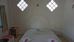 A hotel room with a large bed, two windows with diamond-shaped panes, a bedside table with a phone, and a small wooden stool. - A.P. Garden Hotel (Kalasin)