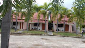 A row of single-story buildings with a red-tiled roof, surrounded by palm trees.