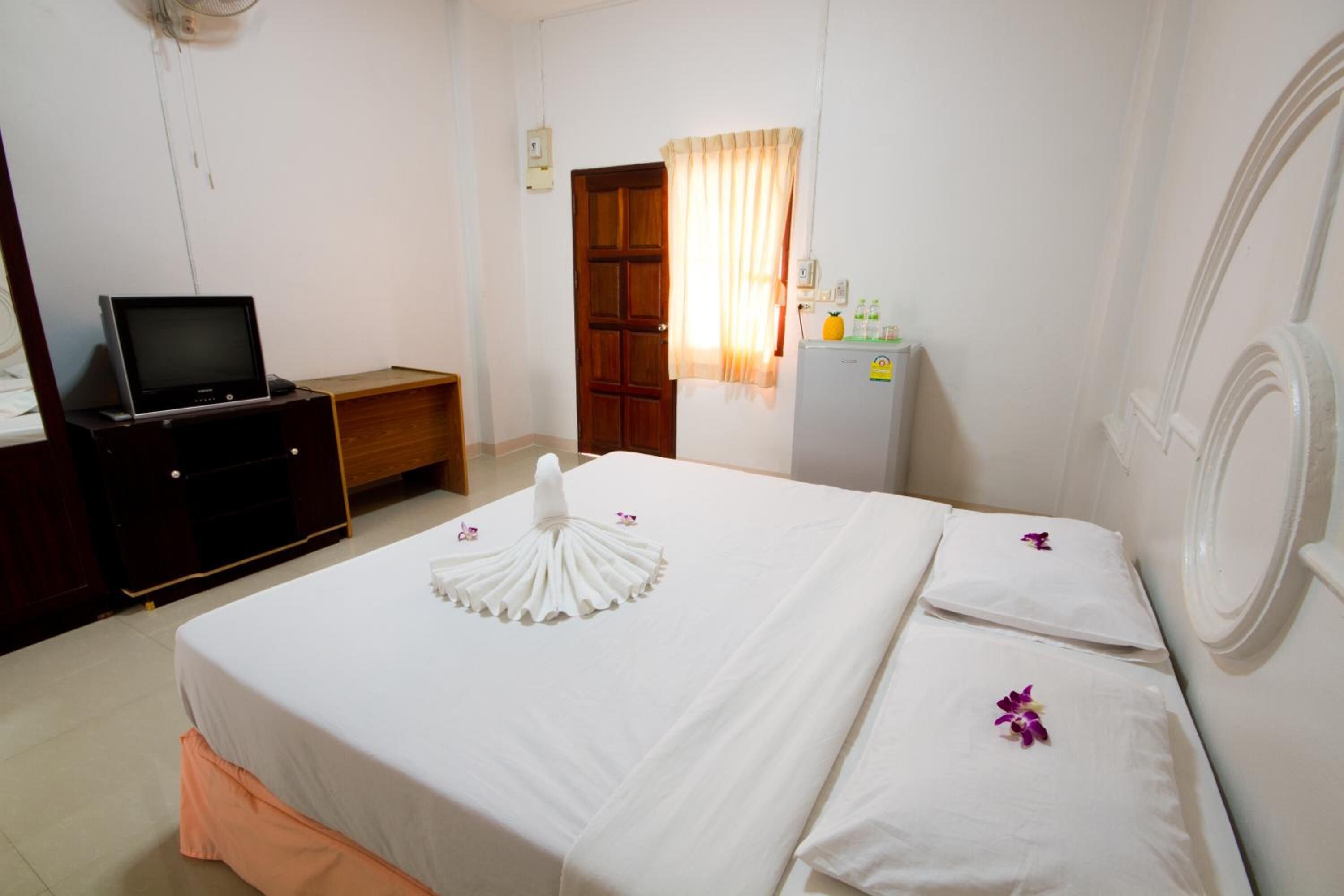 A hotel room with a bed, a television on a stand, a desk, and a refrigerator.