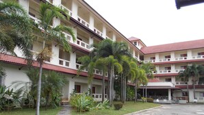 A multi-story building with a red-tiled roof, surrounded by palm trees and greenery. - A.P. Garden Hotel (Kalasin)