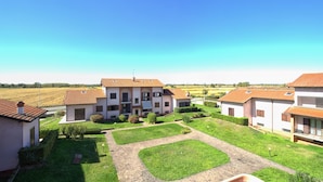 A residential area with a central building featuring a balcony, surrounded by well-maintained gardens and a clear blue sky.