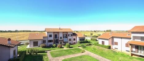 Zona residencial con un edificio central que tiene un balcón, rodeada de jardines cuidados y un cielo azul despejado.