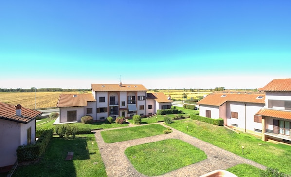 Zona residencial con un edificio central que tiene un balcón, rodeada de jardines cuidados y un cielo azul despejado.