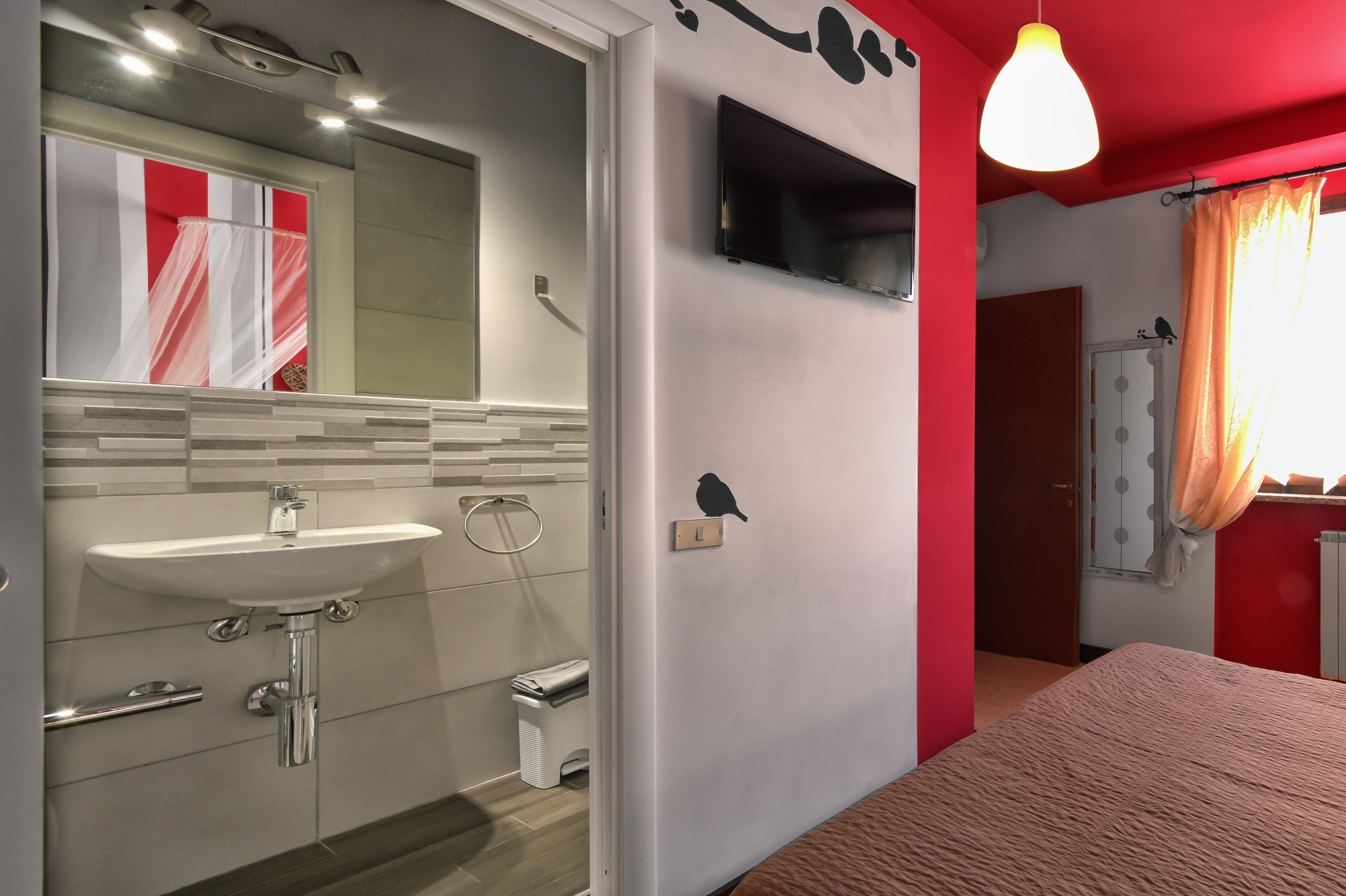 A modern bathroom with a sink, mirror, and shower. A television is mounted on the wall, and a bird decal is visible.
