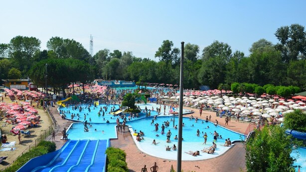 A large outdoor swimming pool area with multiple pools and slides, surrounded by umbrellas and beach chairs.