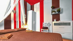 A hotel room with a large bed, a wardrobe, a vanity with a mirror, and a shelf with plants.
