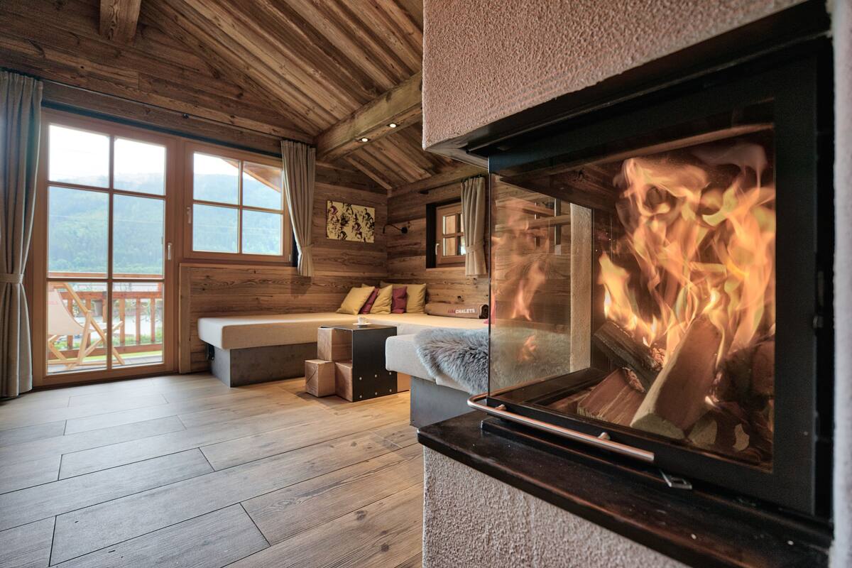 A cozy cabin room with a fireplace, wooden walls, a sofa, and a view of the outdoors.