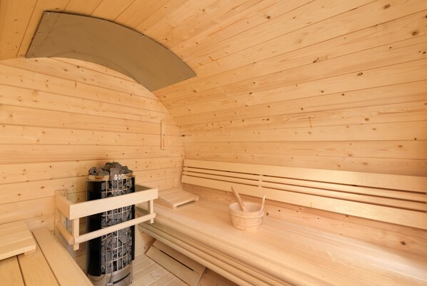 A wooden sauna with benches, a bench seat, a sauna heater, and a wooden bucket. - Lisa Chalets (Flachau)