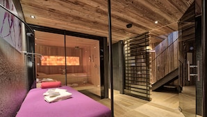 Habitació moderna amb sostre de fusta, separador de vidre, llit amb edredó morat i zona de sauna a la vista.